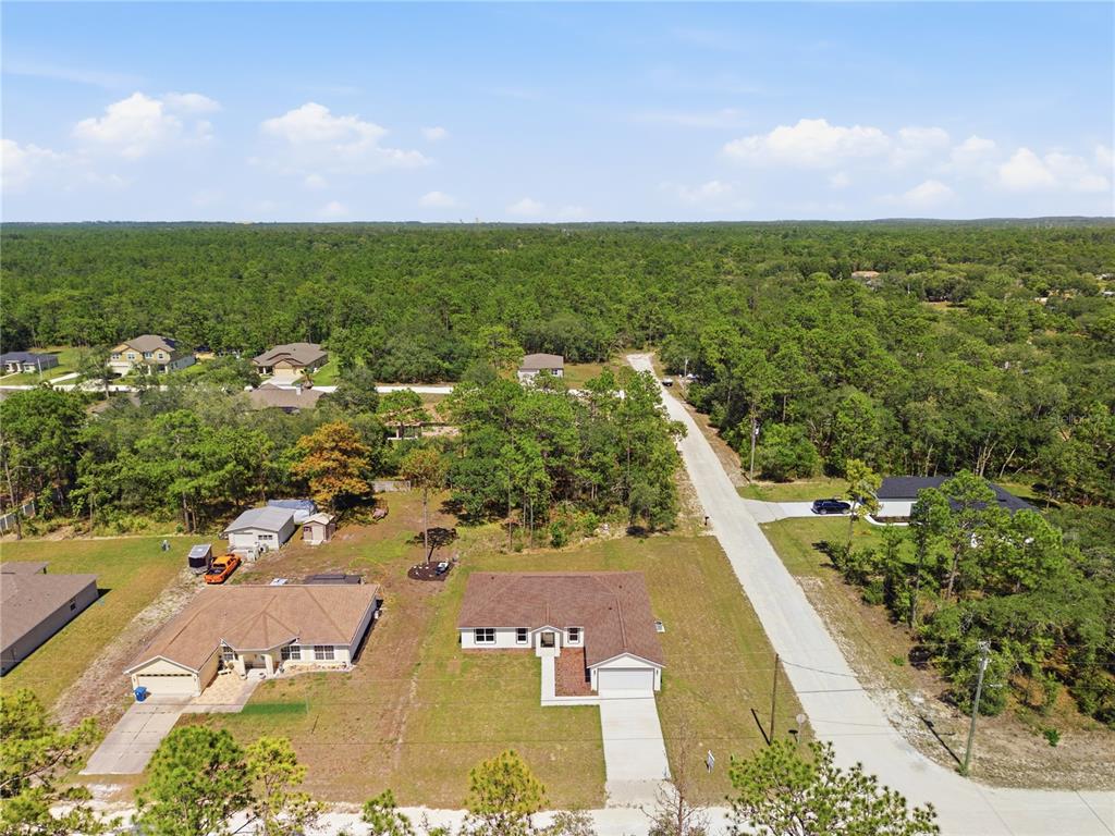 An aerial view shows two suburban houses with driveways surrounded by trees and a road — 14586 MOCKING WREN ROAD, WEEKI WACHEE, FL