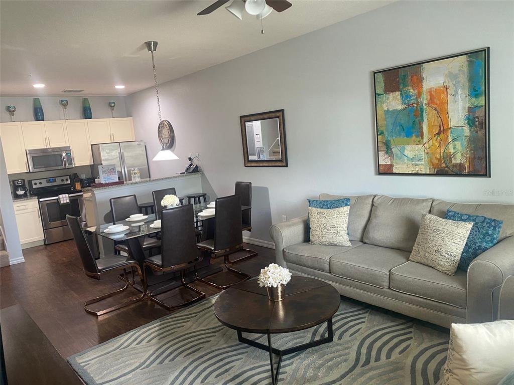 An open-concept living and dining area features a sofa, glass dining table, and kitchen — 3226 WISH AVENUE, KISSIMMEE, FL