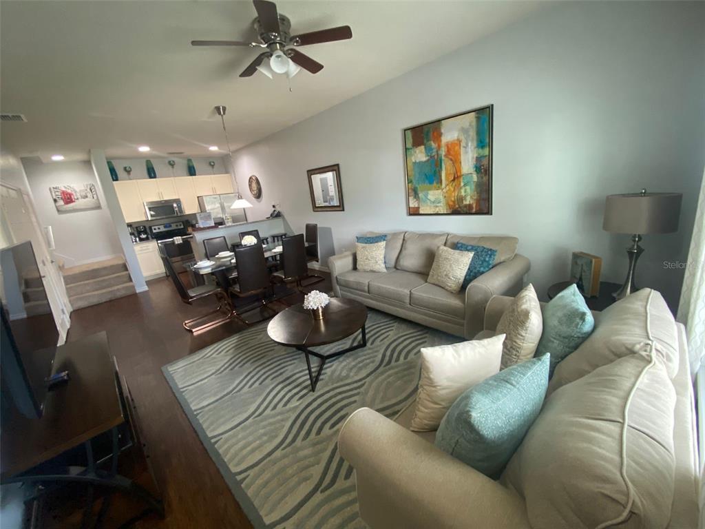 An open-concept living and dining area features a neutral sofa, area rug, and kitchen — 3226 WISH AVENUE, KISSIMMEE, FL