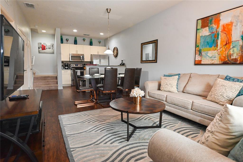An open-concept living and dining area features hardwood floors, a beige sofa, and kitchen cabinetry — 3226 WISH AVENUE, KISSIMMEE, FL