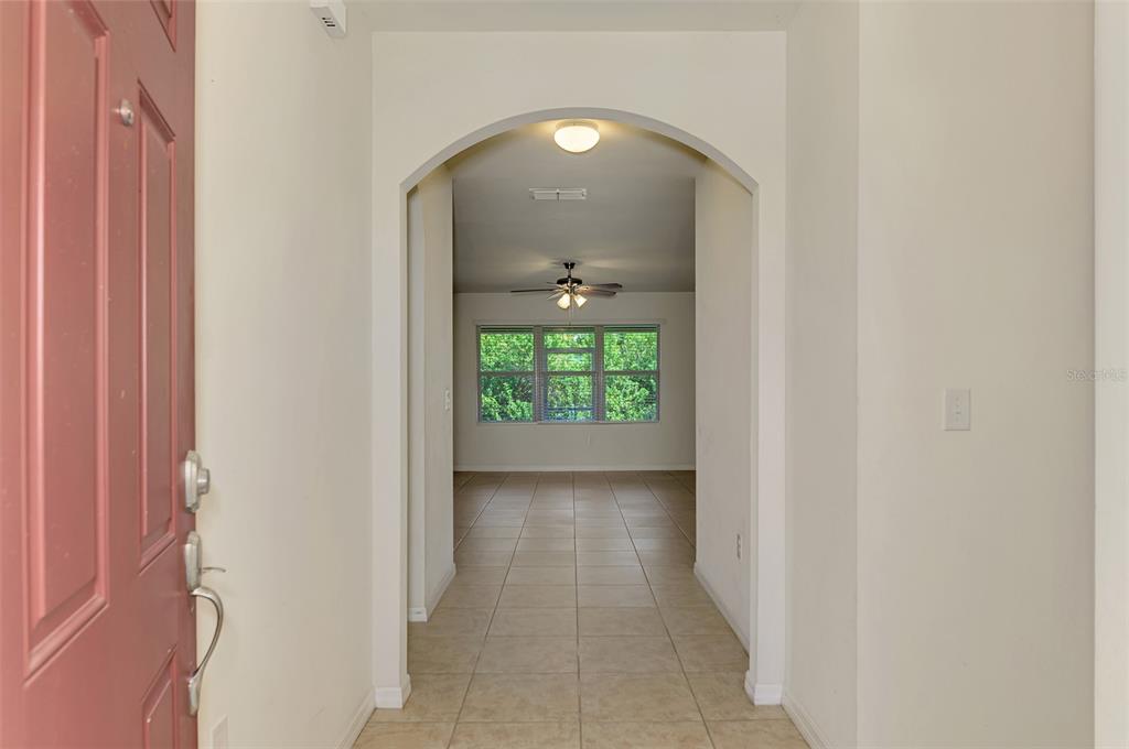 A view from an entryway through an arched doorway into a tiled living area — 10476 HARLINGEN STREET, PORT CHARLOTTE, FL