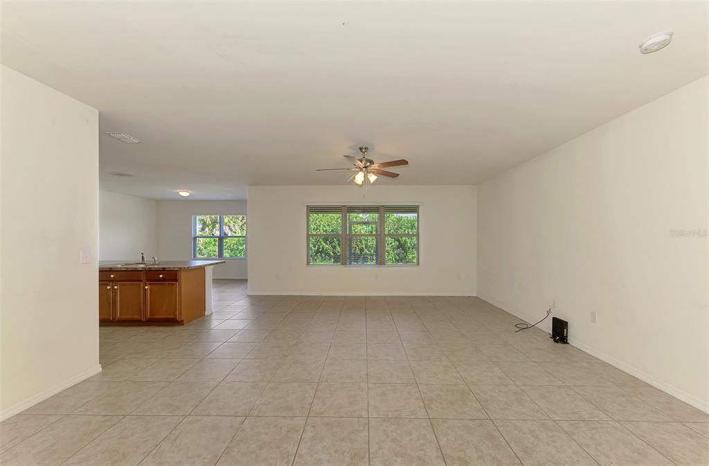 A spacious living area with tile flooring, a ceiling fan, and an adjacent kitchen — 10476 HARLINGEN STREET, PORT CHARLOTTE, FL