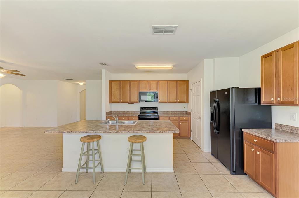 A kitchen features wood cabinets, a black refrigerator, a central island, and tile flooring — 10476 HARLINGEN STREET, PORT CHARLOTTE, FL