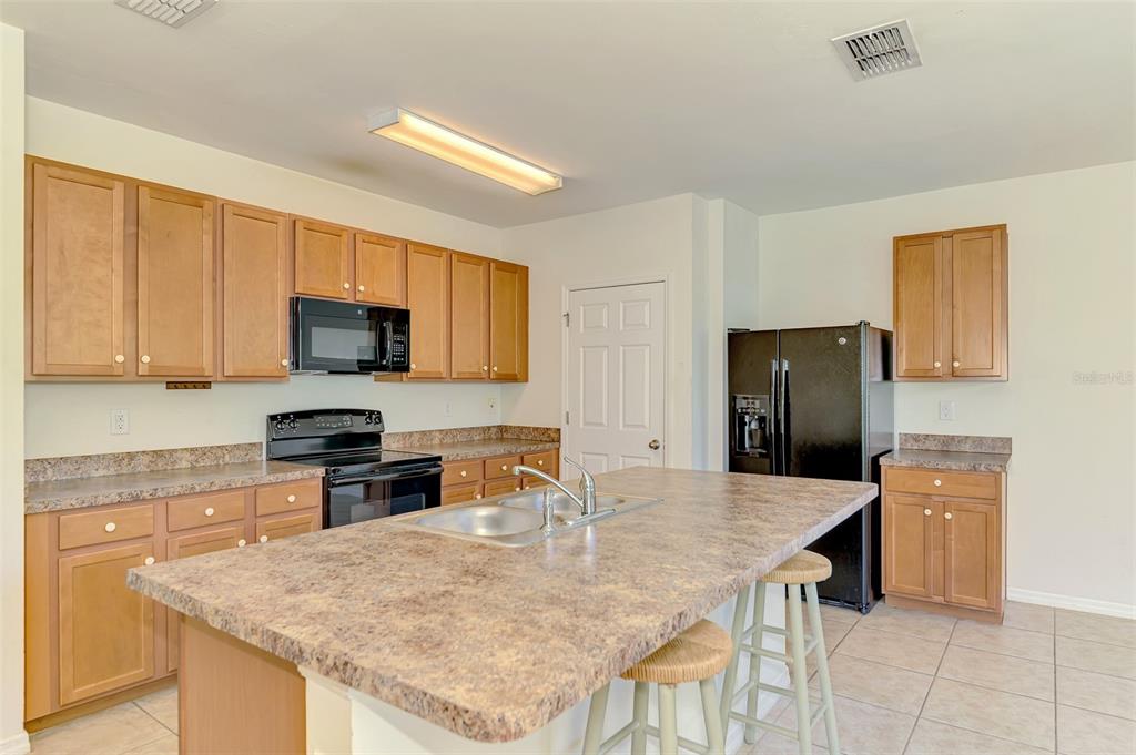 A kitchen with light wood cabinets, laminate countertops, a center island, and black appliances — 10476 HARLINGEN STREET, PORT CHARLOTTE, FL