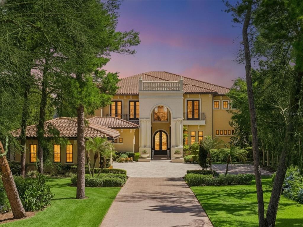 A large Mediterranean-style house with a tile roof and a paved driveway surrounded by trees — 16619 AREZO COURT, MONTVERDE, FL