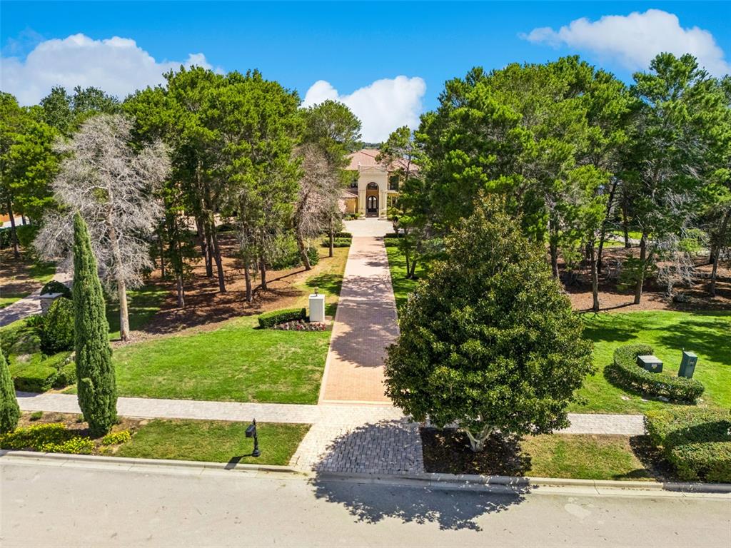 A long brick driveway leads through a wooded yard to a large two-story house — 16619 AREZO COURT, MONTVERDE, FL