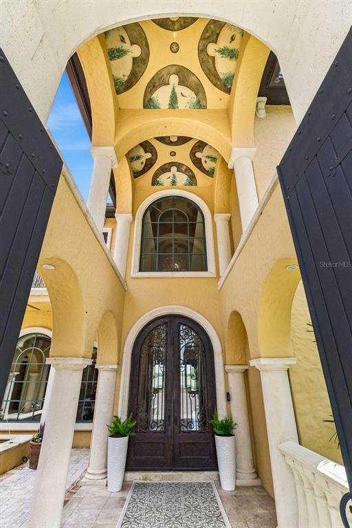 An arched entryway features a painted ceiling, stone columns, and a decorative iron double door — 16619 AREZO COURT, MONTVERDE, FL