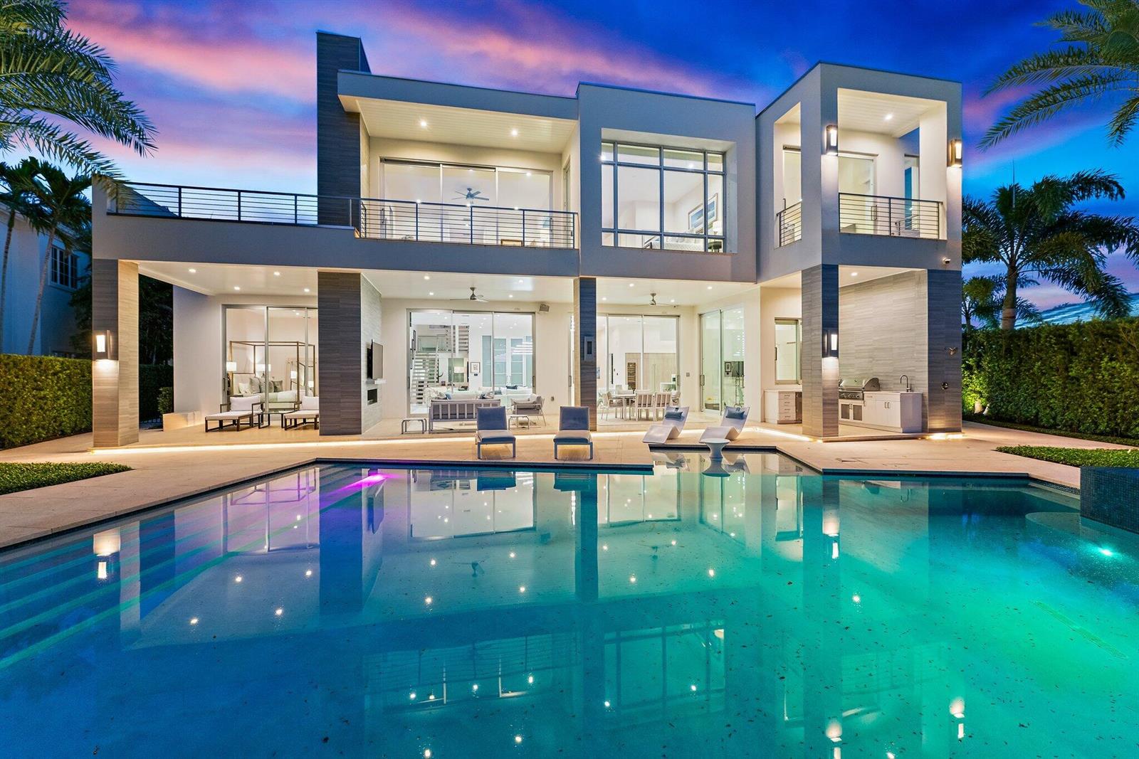 A modern two-story house with a swimming pool, patio, and large glass sliding doors at dusk — 2162 Radnor Road, North Palm Beach FL 33408, NORTH PALM BEACH, FL