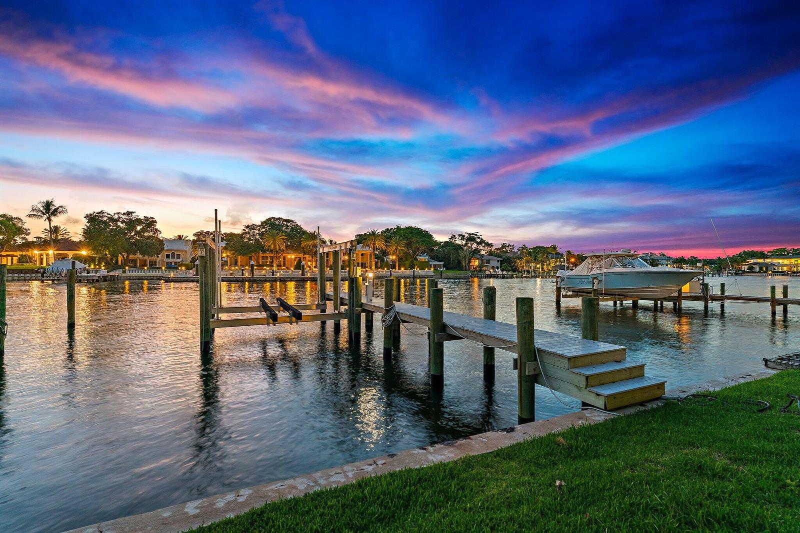 A wooden boat dock extends into a canal at sunset with a boat moored nearby — 2162 Radnor Road, North Palm Beach FL 33408, NORTH PALM BEACH, FL