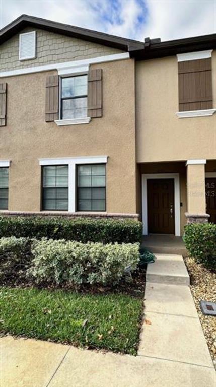 A two-story townhouse exterior features tan stucco walls, brown shutters, and a manicured hedge — 4393 FENNWOOD CT, WESLEY CHAPEL, FL