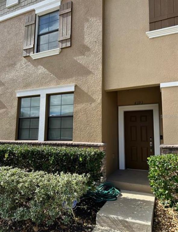 A two-story tan townhouse exterior features brown shutters, a dark front door, and manicured landscaping — 4393 FENNWOOD CT, WESLEY CHAPEL, FL