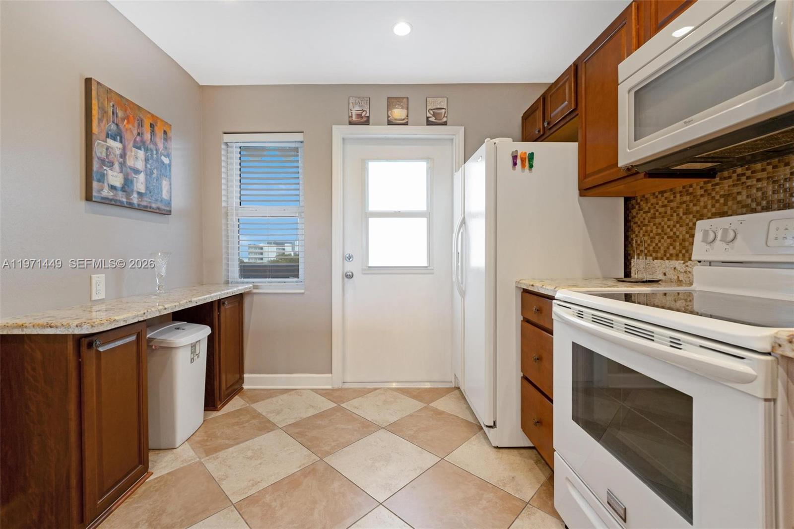 A kitchen features wood cabinets, white appliances, granite countertops, and a tiled floor — 1000 NE 14th Ave # 602, Hallandale Beach FL 33009, HALLANDALE BEACH, FL
