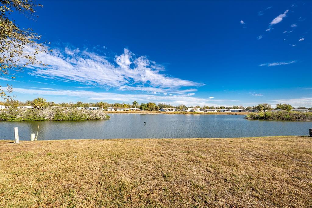 A grassy lawn overlooks a lake with distant houses under a blue sky — 1300 SANDERLING DRIVE, ENGLEWOOD, FL