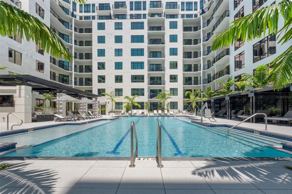 A swimming pool with lounge chairs and palm trees sits in a modern apartment courtyard — 1991 MAIN STREET Aster B6, SARASOTA, FL
