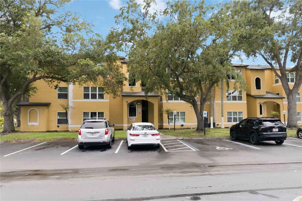 A three-story yellow apartment building stands behind a parking lot with three parked cars — 4572 COMMANDER DRIVE UNIT 1227, ORLANDO, FL