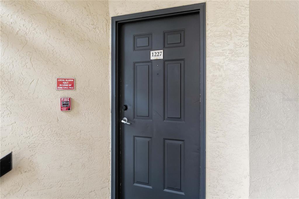 A dark gray six-panel door with the number 1227 is set in a textured beige wall — 4572 COMMANDER DRIVE UNIT 1227, ORLANDO, FL