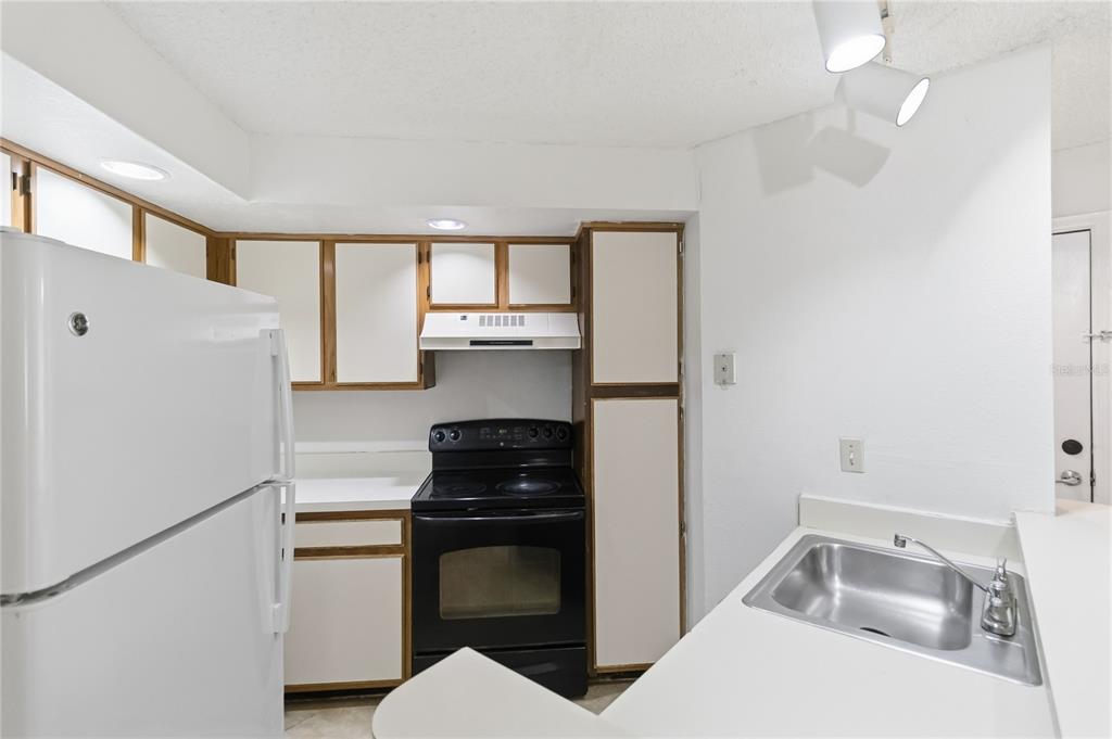 A kitchen features white cabinets, a black stove, a white refrigerator, and a stainless sink — 4572 COMMANDER DRIVE UNIT 1227, ORLANDO, FL