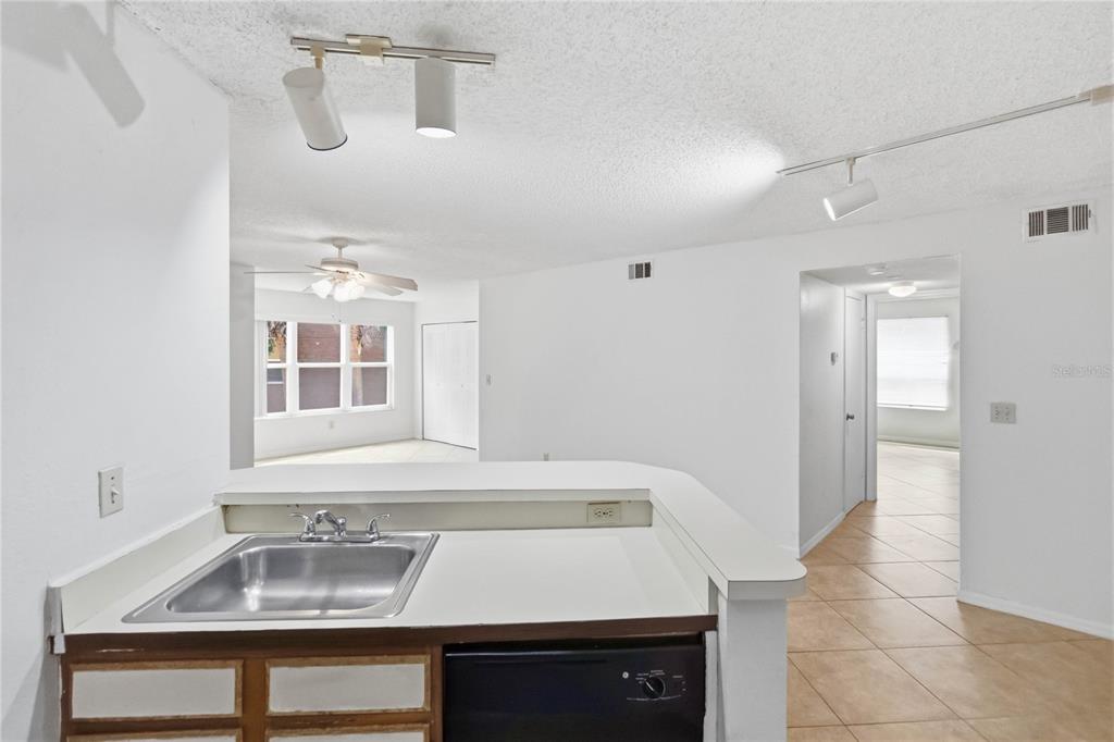 A kitchen sink and counter overlook a living area with white walls and tile flooring — 4572 COMMANDER DRIVE UNIT 1227, ORLANDO, FL