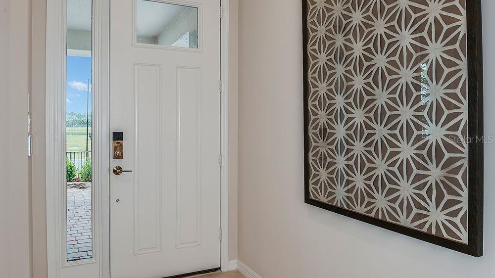 A white front door with a side window sits next to a geometric wall art piece — 3444 LUMBER FALLS DRIVE, PLANT CITY, FL