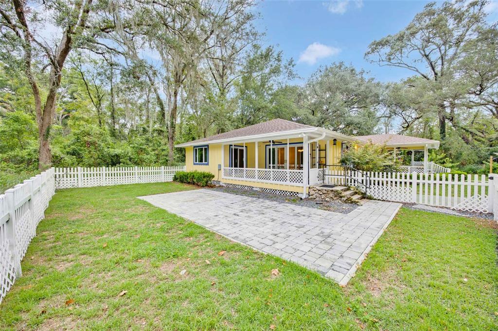 A yellow house with a screened porch and a paved patio sits behind a white fence — 19922 NW 131ST PLACE, ALACHUA, FL
