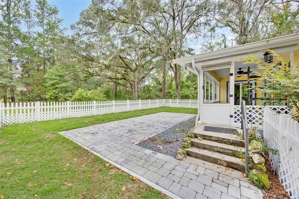 A backyard features a paved patio, a white picket fence, and a screened-in porch — 19922 NW 131ST PLACE, ALACHUA, FL