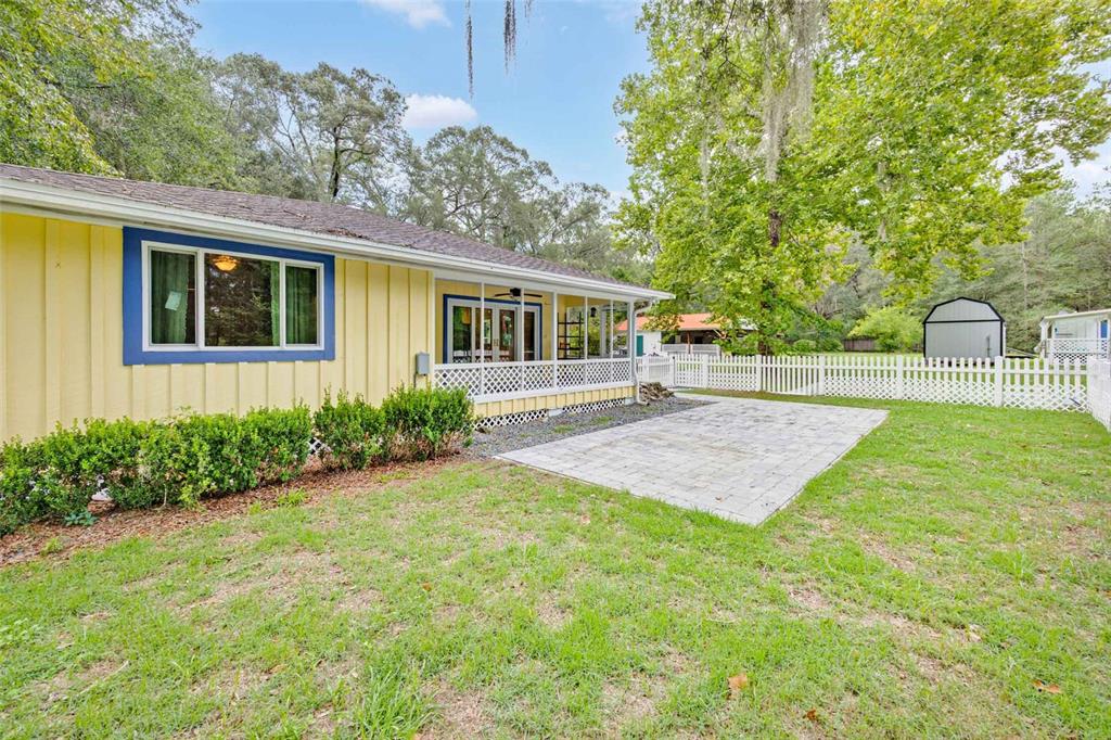 The exterior of a yellow house features a screened porch, a paver patio, and fencing — 19922 NW 131ST PLACE, ALACHUA, FL