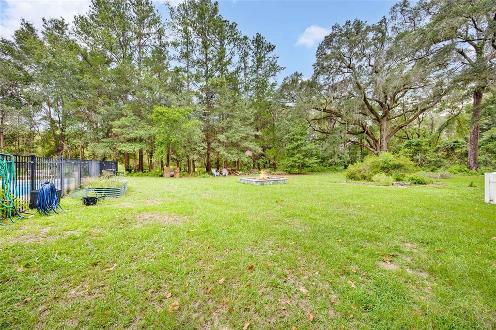 A grassy backyard features a stone fire pit, a black metal fence, and mature trees — 19922 NW 131ST PLACE, ALACHUA, FL