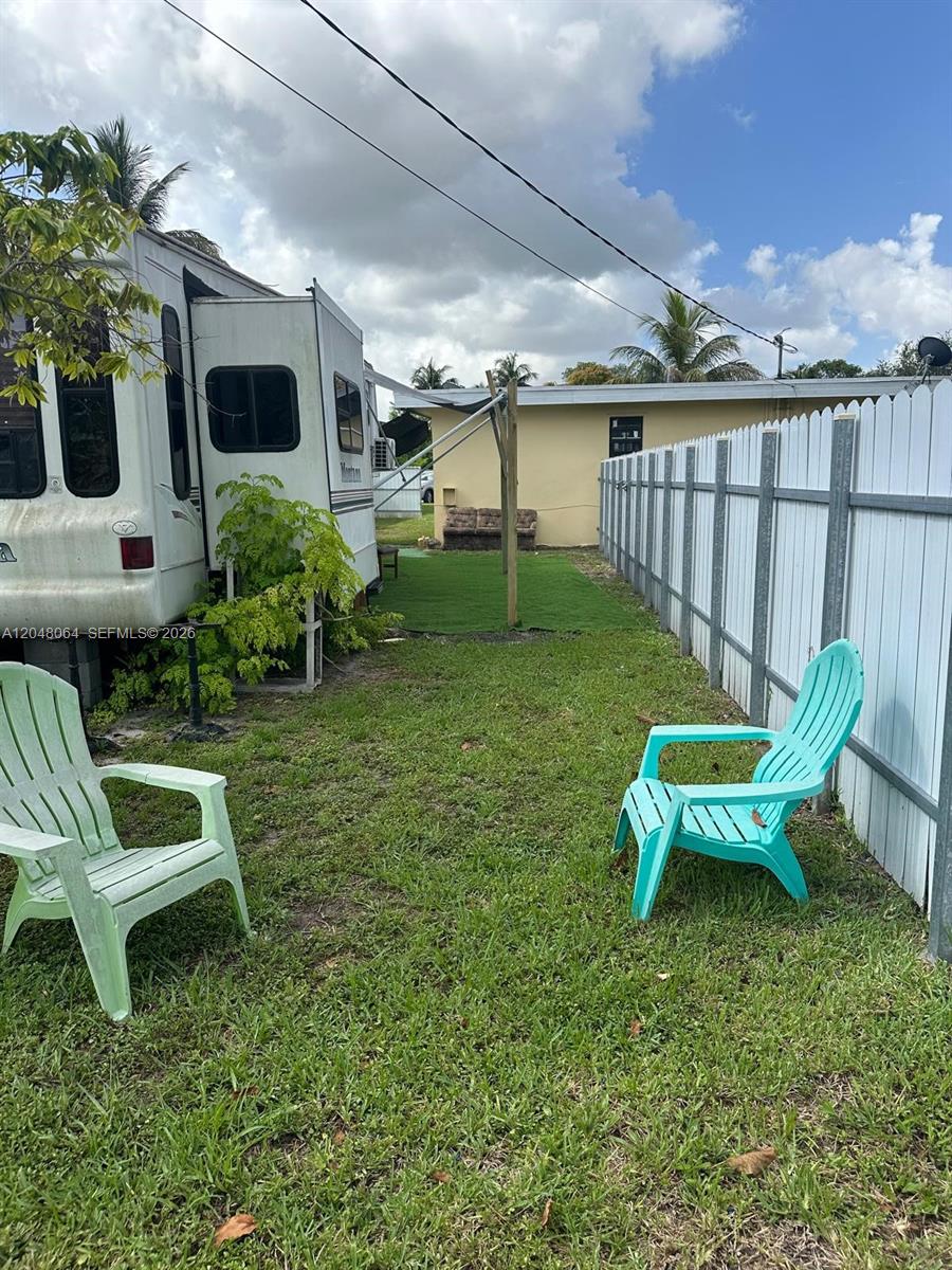 A grassy backyard features two plastic chairs, a wooden fence, and a small tree — 655 NW 152nd St # 655, Miami FL 33169, MIAMI, FL