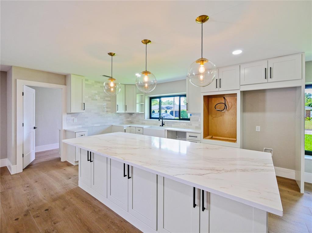 A modern kitchen features white cabinetry, a large marble-topped island, and stainless steel appliances — 2491 LAUDER DRIVE, MAITLAND, FL