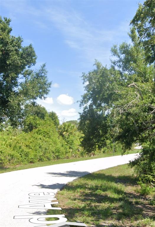A paved road curves through a wooded area under a clear blue sky — 12343 SUNNILAND AVENUE, PORT CHARLOTTE, FL