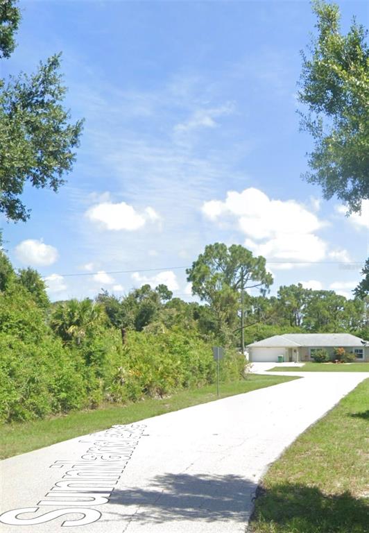 A paved driveway leads toward a single-story house surrounded by trees and dense vegetation — 12343 SUNNILAND AVENUE, PORT CHARLOTTE, FL
