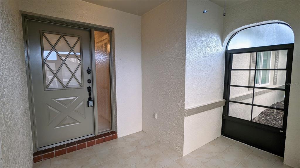 A covered entryway features a light-colored front door, tiled flooring, and a screened-in window — 1624 LAYTON COURT UNIT 1624, SUN CITY CENTER, FL