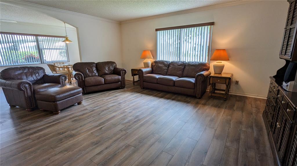 A living room features brown leather furniture, wood-look flooring, and two windows with blinds — 1624 LAYTON COURT UNIT 1624, SUN CITY CENTER, FL