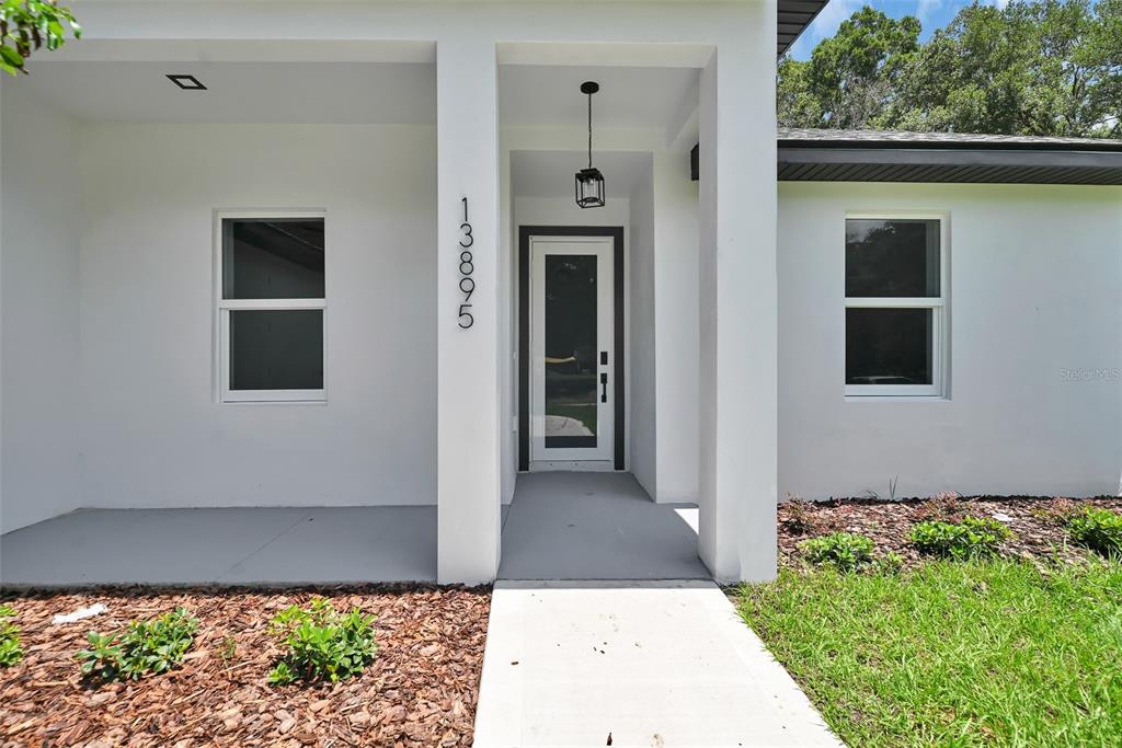 The exterior of a white house features a front porch, a glass-paneled door, and windows — 13895 SW 110TH PLACE, DUNNELLON, FL