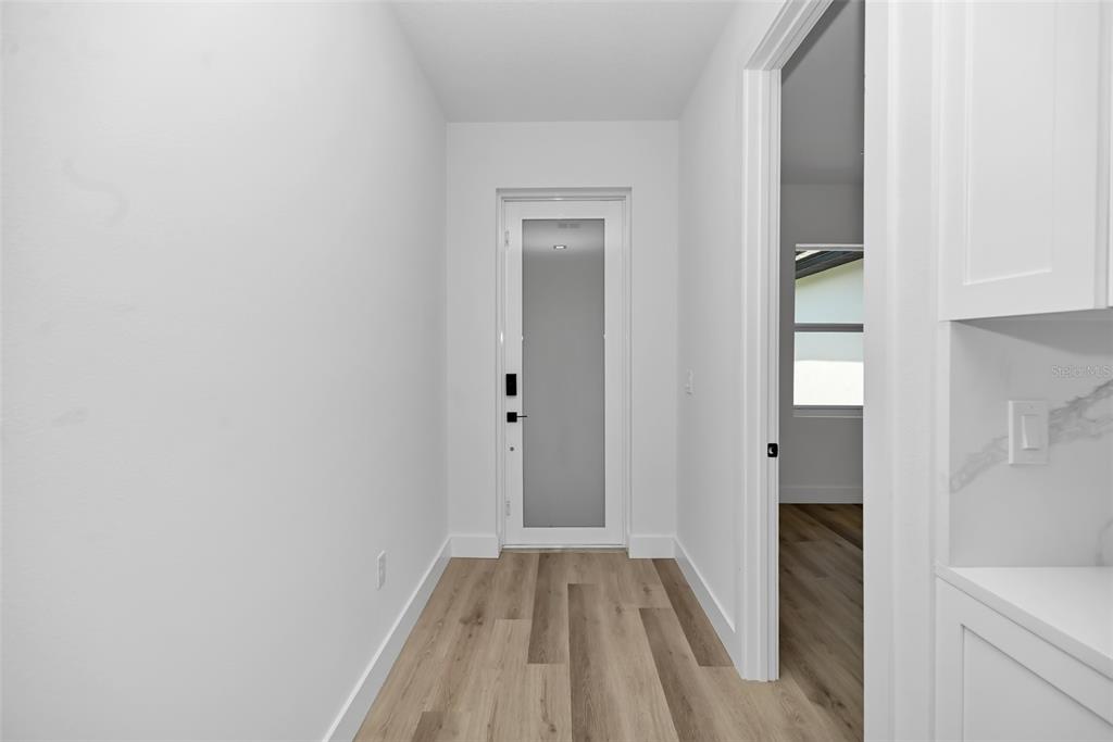 A hallway with light wood-look flooring leads to a door with a frosted glass panel — 13895 SW 110TH PLACE, DUNNELLON, FL