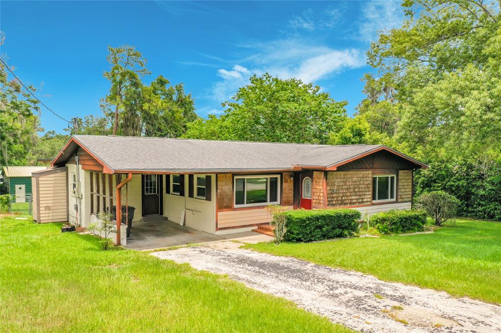 A single-story house with a carport, wood-shingle siding, and a concrete driveway on a lawn — 2405 NE 2ND STREET, OCALA, FL