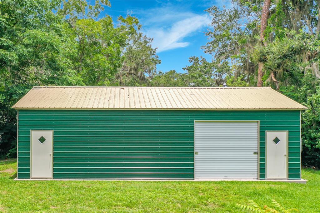 A green metal storage building with a tan roof, a roll-up door, and two side doors — 2405 NE 2ND STREET, OCALA, FL