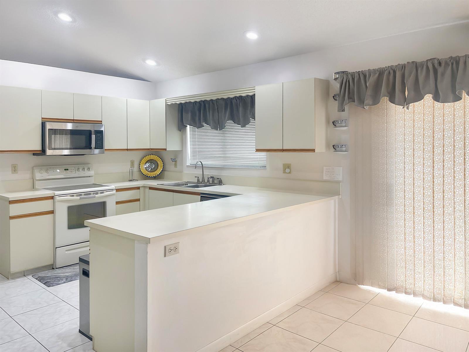 A kitchen features white cabinets, a peninsula countertop, a white stove, and a sliding door — 9525 El Clair Ranch Road, Boynton Beach FL 33437, BOYNTON BEACH, FL