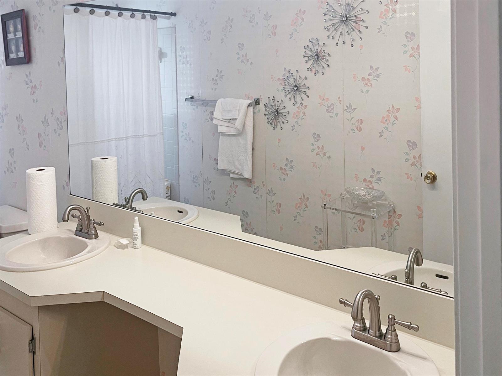 A bathroom with a double vanity, floral wallpaper, and a large wall-to-wall mirror — 9525 El Clair Ranch Road, Boynton Beach FL 33437, BOYNTON BEACH, FL