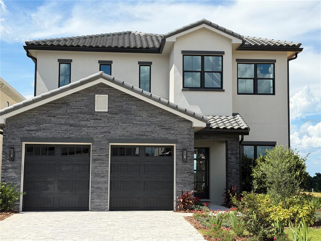 A two-story house with a stone-veneer facade, two garage doors, and a tiled roof — 15825 VETTA DRIVE, BELLA COLLINA, FL