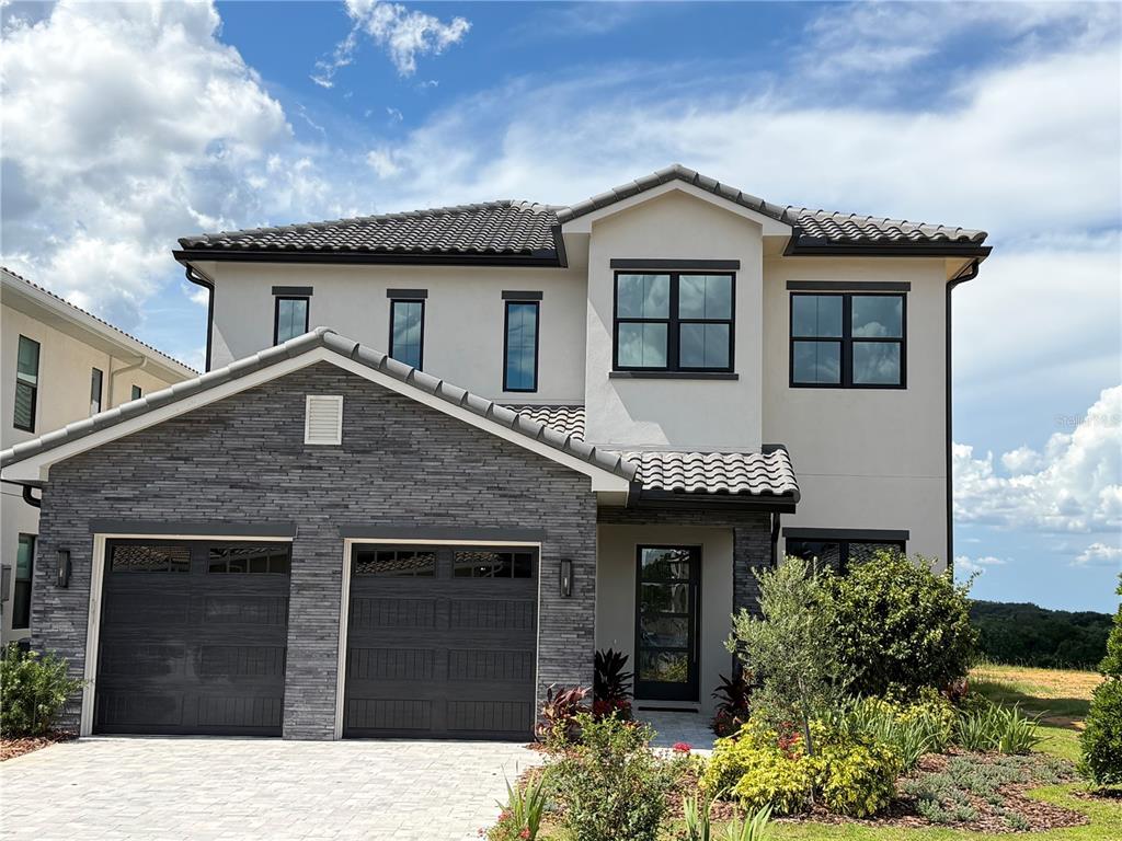 A two-story house features a stone-veneer garage, a tiled roof, and a glass-paneled front door — 15825 VETTA DRIVE, BELLA COLLINA, FL