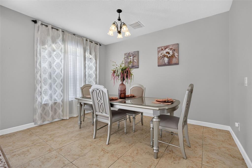 A dining room features a glass-topped table, four chairs, a chandelier, and tile flooring — 1766 OAK GROVE CHASE DRIVE, ORLANDO, FL
