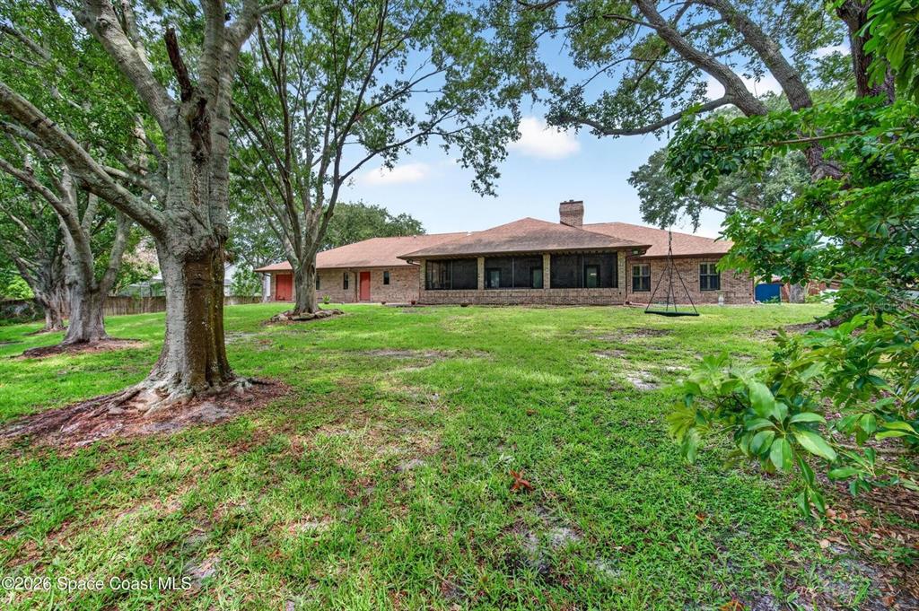 A brick house with a screened-in porch sits on a large, tree-filled grassy lot — 415 CHEYENNE TRAIL, MERRITT ISLAND, FL