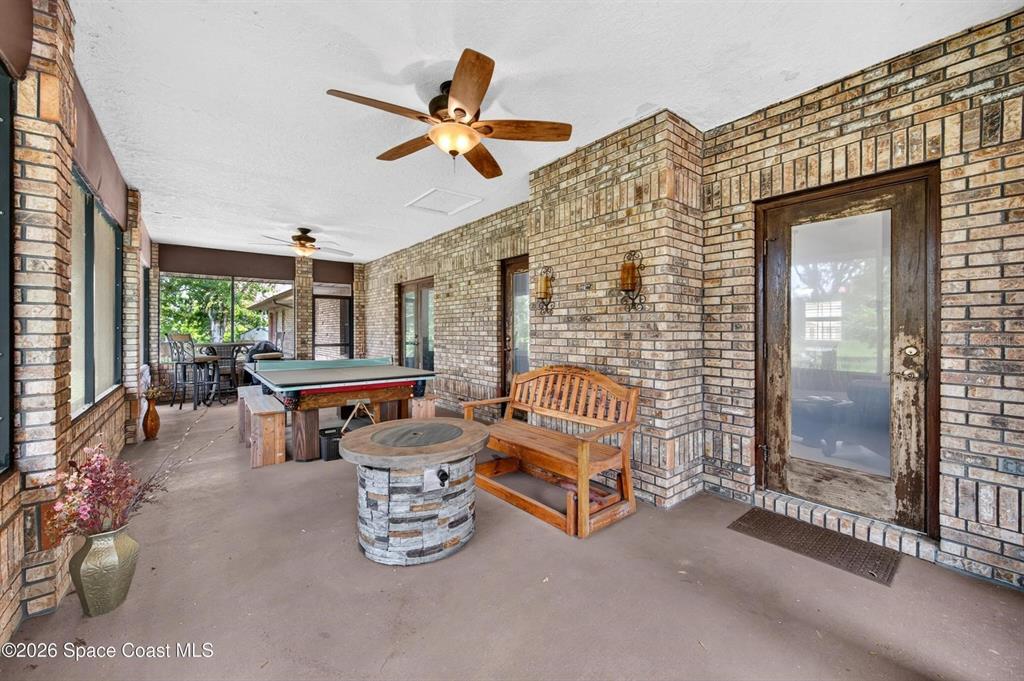 A covered brick patio features a wooden bench, a fire pit, and a ping pong table — 415 CHEYENNE TRAIL, MERRITT ISLAND, FL