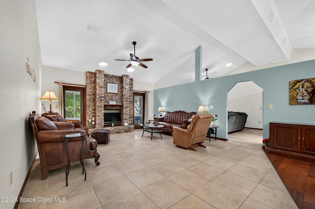 A living room features a brick fireplace, vaulted ceilings, tile flooring, and leather furniture — 415 CHEYENNE TRAIL, MERRITT ISLAND, FL