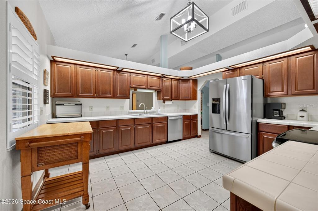 A kitchen features wood cabinets, stainless steel appliances, tile flooring, and a vaulted ceiling — 415 CHEYENNE TRAIL, MERRITT ISLAND, FL