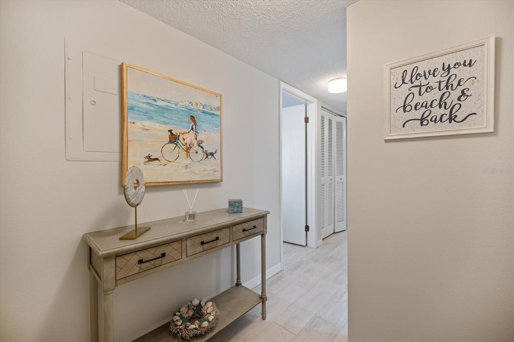 A hallway features a wooden console table, a beach-themed painting, and wall art — 1604 STICKNEY POINT ROAD UNIT 102, SARASOTA, FL