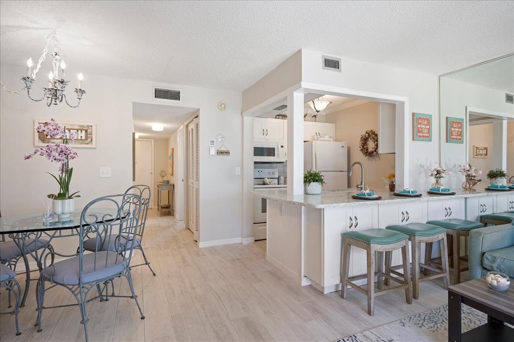 A dining area and kitchen with a breakfast bar, light wood flooring, and white cabinetry — 1604 STICKNEY POINT ROAD UNIT 102, SARASOTA, FL