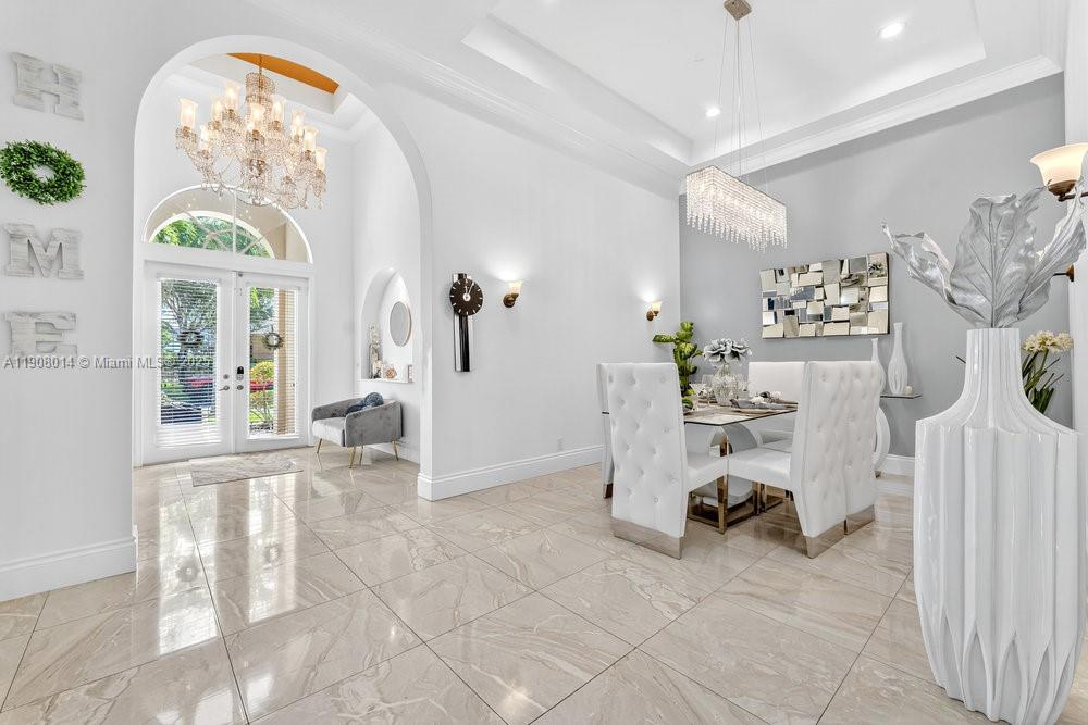 A bright dining area features white tufted chairs, a crystal chandelier, and polished tile floors — 6313 Paradise Cv, West Palm Beach FL 33411, WEST PALM BEACH, FL