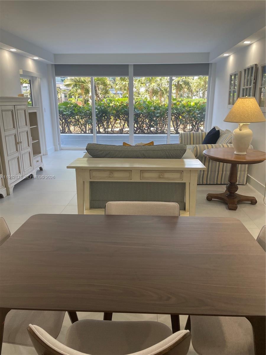 A dining area in the foreground overlooks a living room with large windows and greenery — 10275 Collins Ave # 208, Bal Harbour FL 33154, BAL HARBOUR, FL